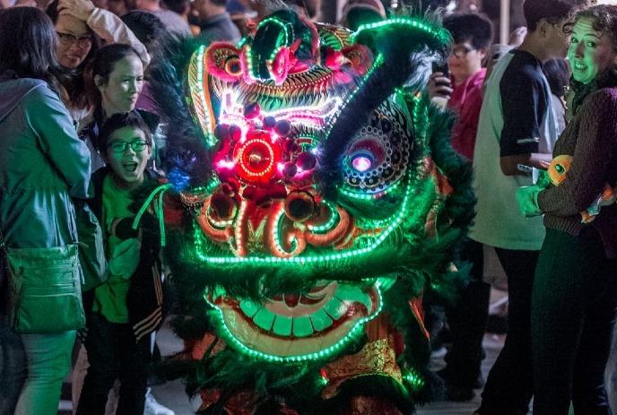 People surrounding a lit up giant dragon costume at night.