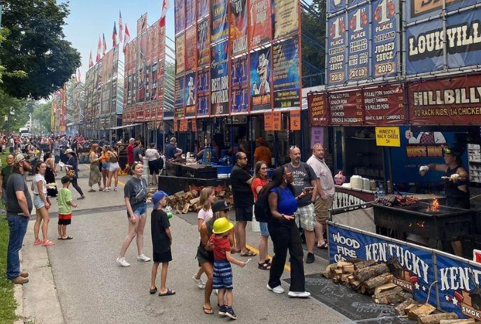 Ribfest with food stalls, colorful banners, grilling meat, and crowds enjoying the event.
