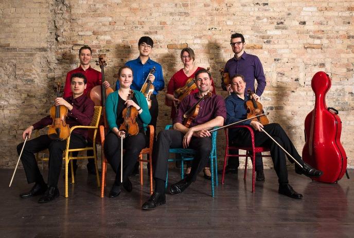 Group of musicians sit onstage together with their instruments.