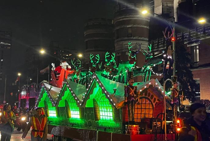 Float with a Christmas inspired house on top with snow and reindeer.