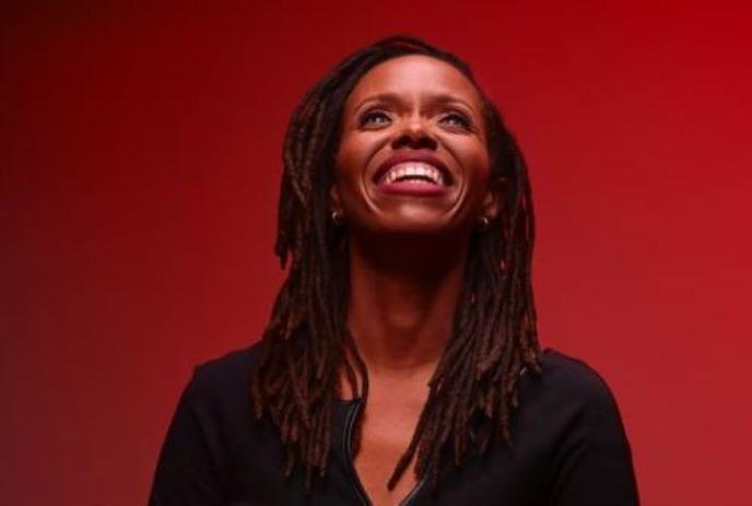 Artist smiling and looking upwards in a black dress under a red background.