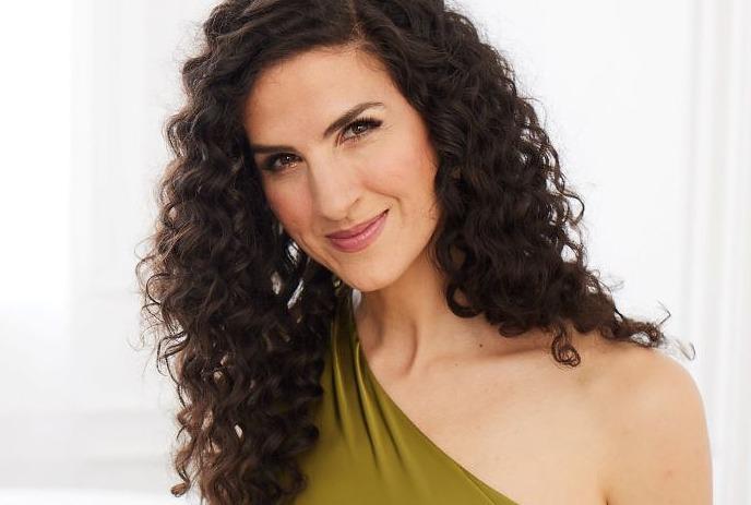 Laila Biali smiling wearing a green dress, in front of a white background.