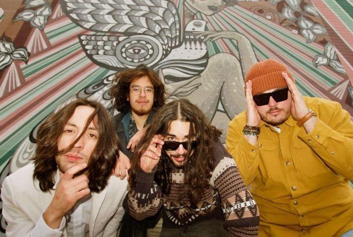 Four artists stand before a vibrant mural with wings, patterns and flowers.,