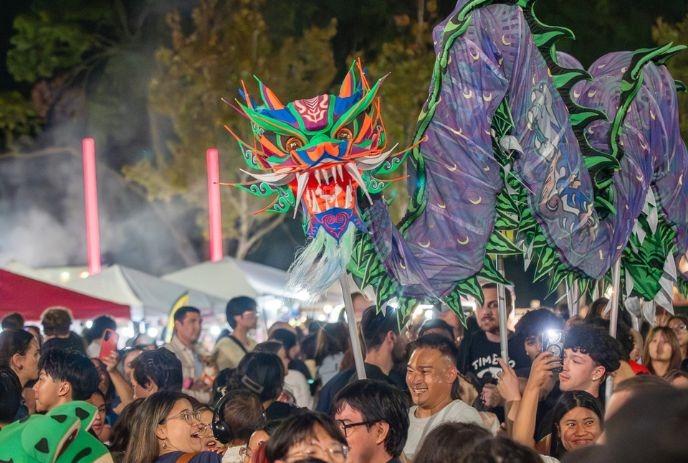 Crowds gather before bright stage with lion banner festive colors families watching lively cultural celebration.