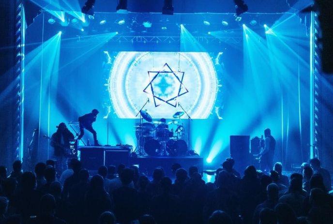 Parabolus performing on stage in front of a crowd, surrounded by blue light.
