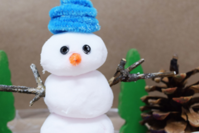 White pom-pom snowman with blue pipe cleaner hat and two twigs for arms.
