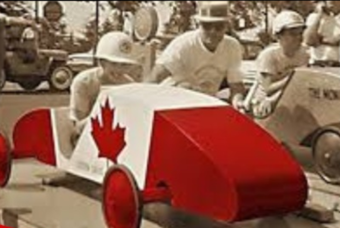 Red and white soapbox car with maple leaf, with people in sepia behind it.