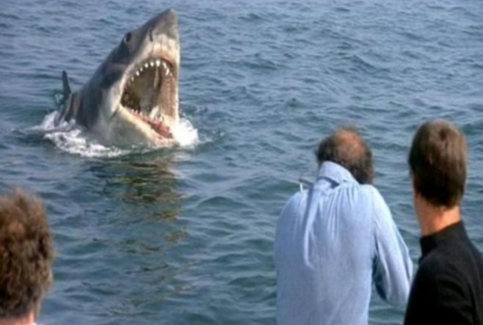 A shark with mouth wide open coming up out of the water towards some people.