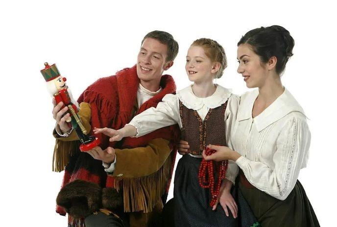 A smiling family admires a colorful nutcracker, sharing a joyful holiday moment together in traditional attire.