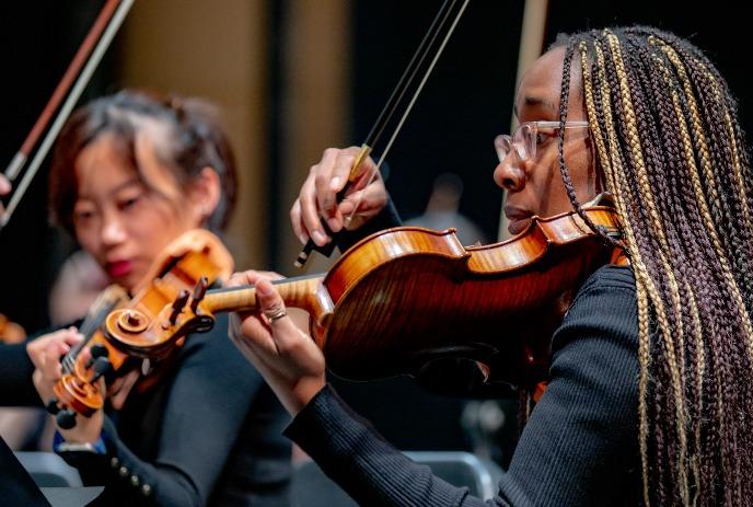 Two violinists in black suites, perform with bows raised with the blurred background.