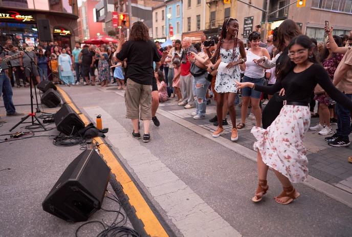 Crowd dancing to live street music, people smiling and moving as performers play on a warm urban evening.