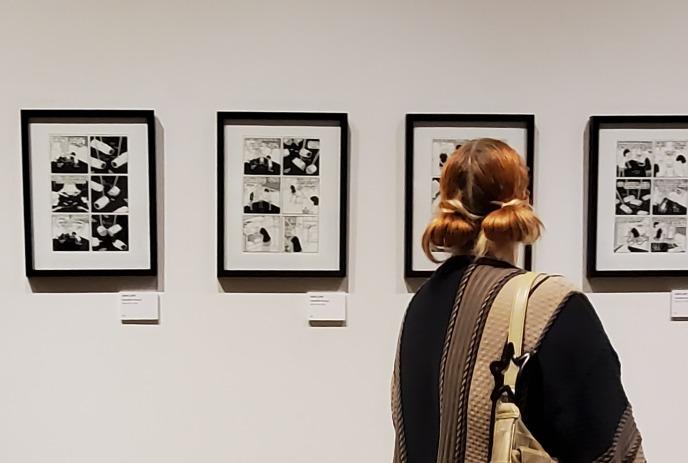 Women focusing on the framed black and white comic panels on a gallery wall during an art exhibit.