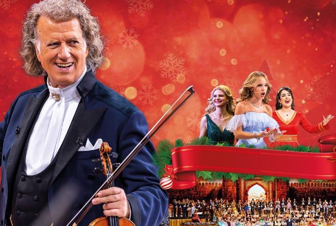 André Rieu holding a violine, with people in the background singing.