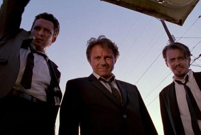 Three suited men stand beneath a structure, gazing downward; clear sky and power lines fill the backdrop.