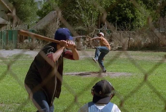 Three people playing baseball as seen from the fence behind first base.