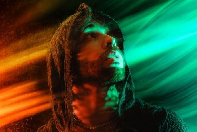 Ero808 in a hood gazes upwards, enveloped in swirling red and green light effects.