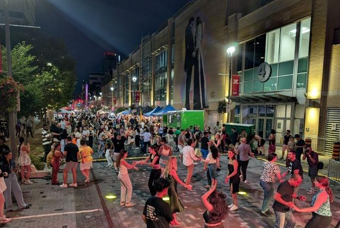 Night street festival crowd dancing under warm lights with mural backdrop creating lively energy.