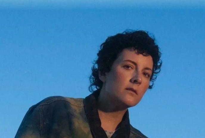 Ria Mae gazes ahead with a calm, reflective expression, wearing a denim jacket and short curls.
