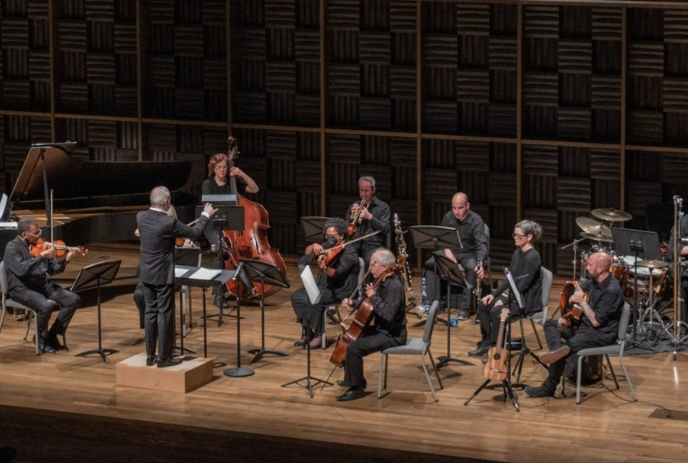 Orchestra on stage with conductor standing in front performing.