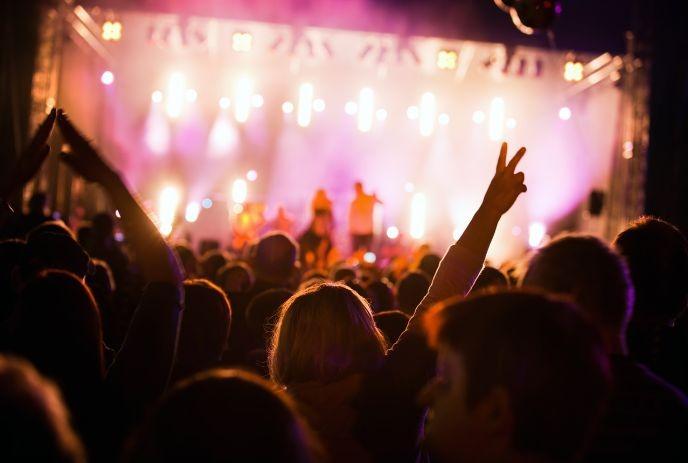 Crowd lifts hands toward bright stage lights as music fills night air in vibrant festival scene.