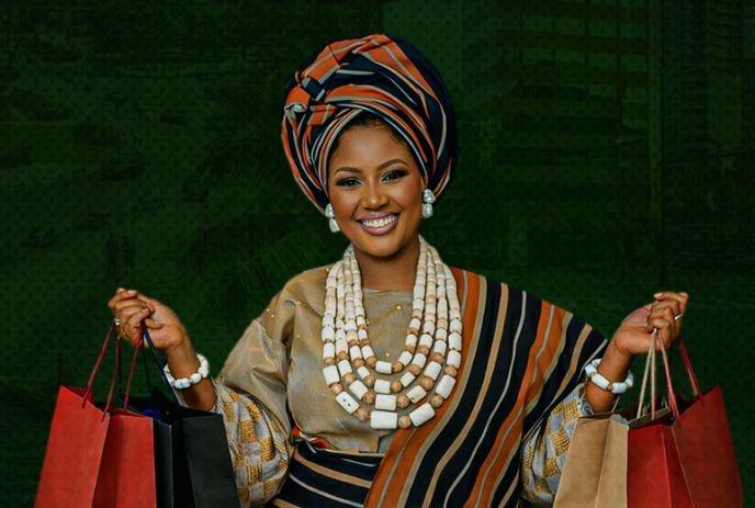 Elegant woman in vibrant African attire holding shopping bags, blending tradition and modern style gracefully.