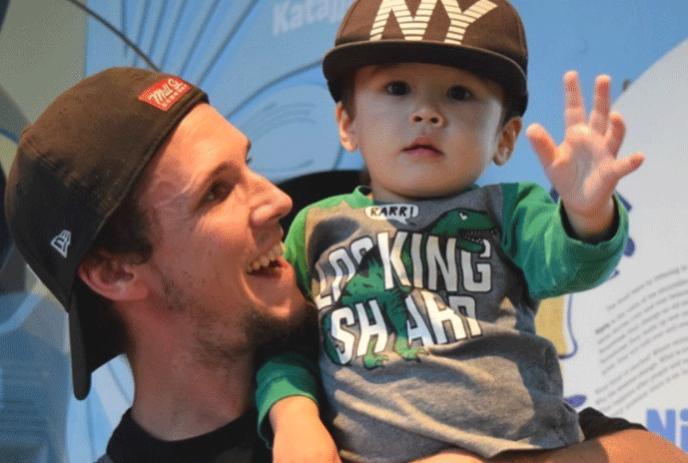 Man with cap on backwards, holding little boy who is smiling.