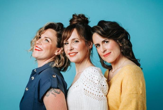 The 3 members of the Good Lovelies posing for the camera in front of a blue wall.