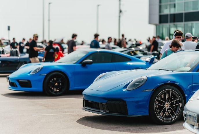 Bright blue sports cars parked together at a lively outdoor car meet with people walking around nearby