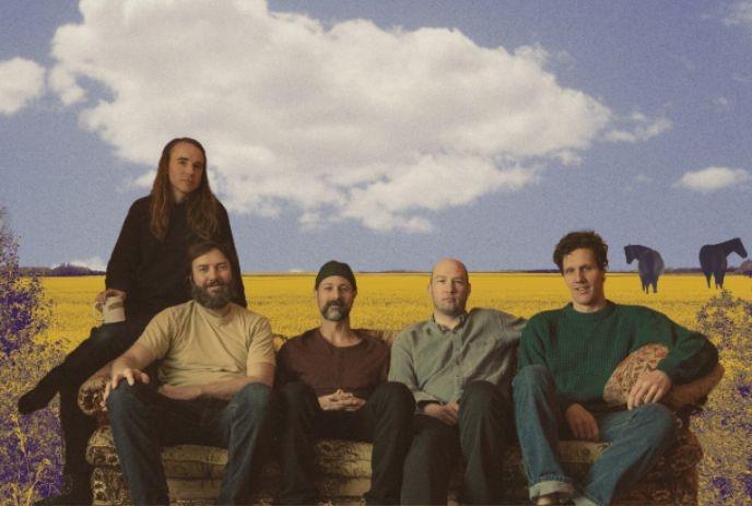 Foxwarren with Hudson Freeman, posed on a vintage couch with golden prairie fields, wildflowers, open sky, and horses.