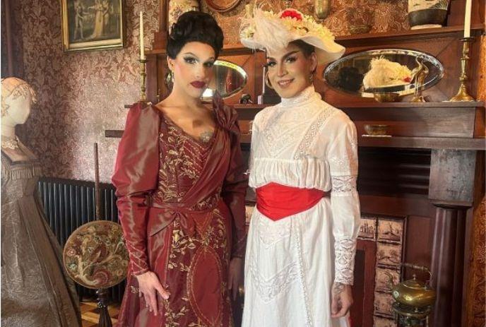 Elegant vintage room with two women in ornate dresses standing before decorated fireplace