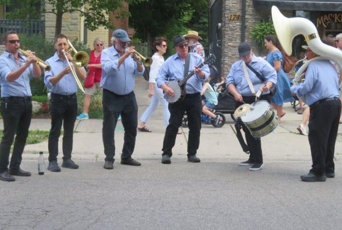 A band wearing blue shirts and black pants plays instruments on the street.
