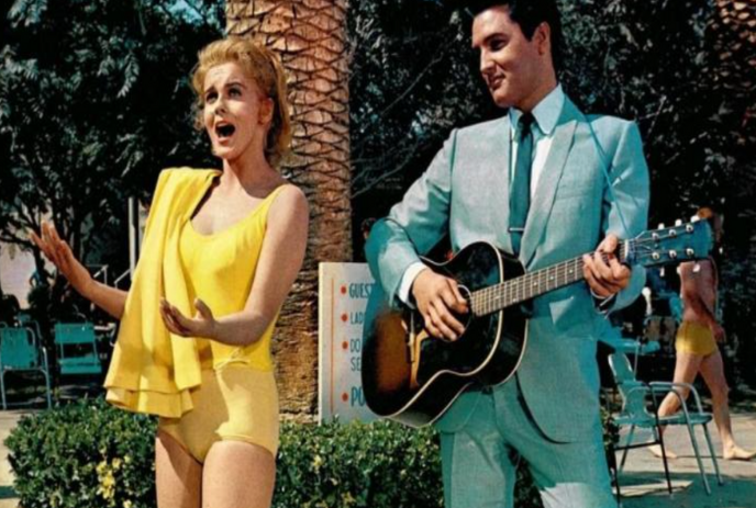 An actress in a yellow bathing suit sings while Elvis Presley plays guitar beside her.