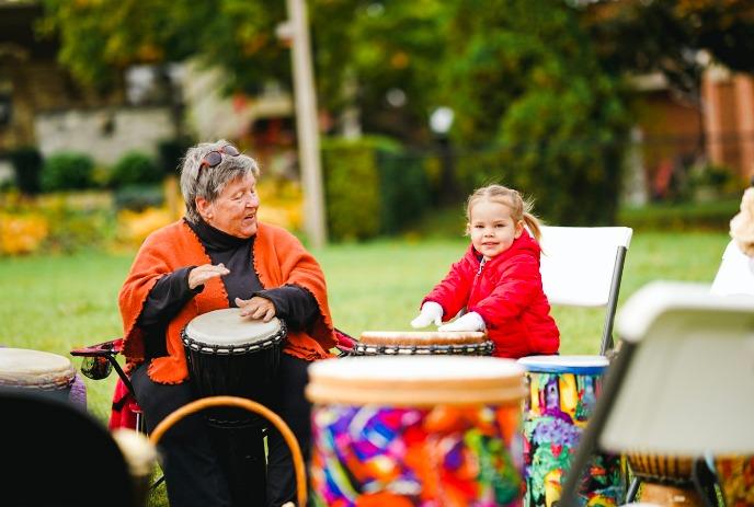 An adult and a child in a drumming circle outside.