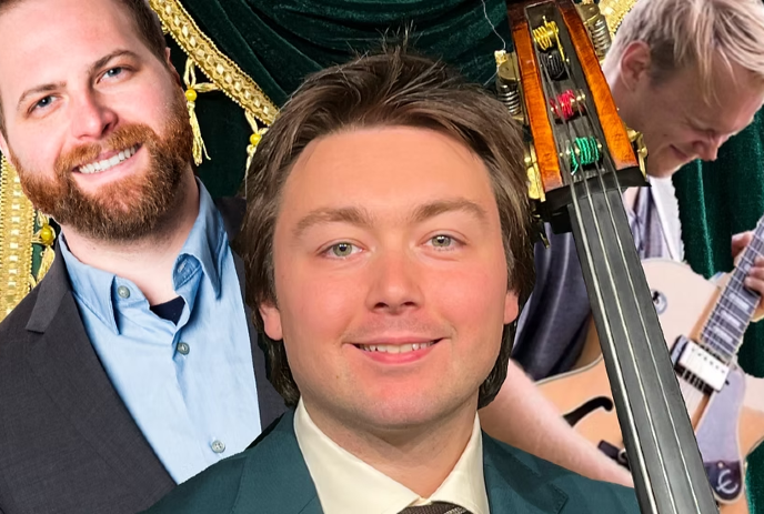 A smiling man in a suit stands in front of musicians playing guitar and an upright bass.