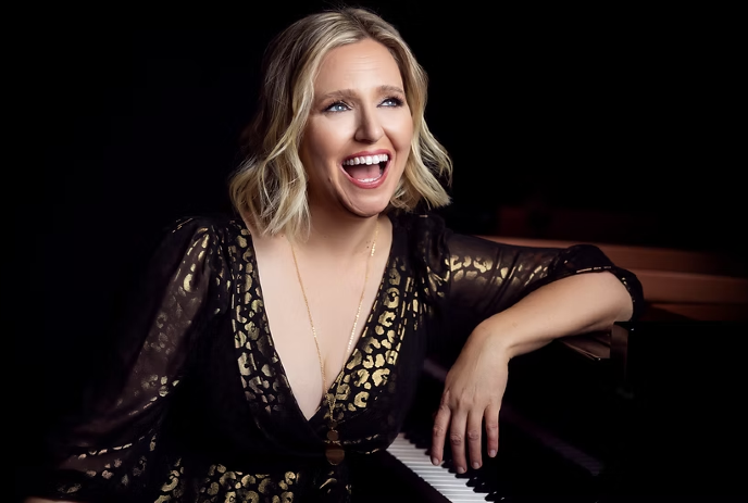Brenda Earle wearing a black dress, smiling while looking upwards in front of a black background.