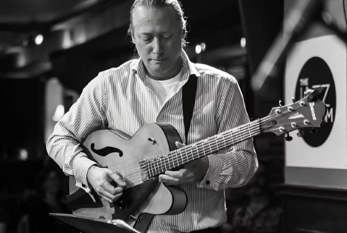 A black and white photo of Andy Tattersall playing guitar on stage for a crowd.