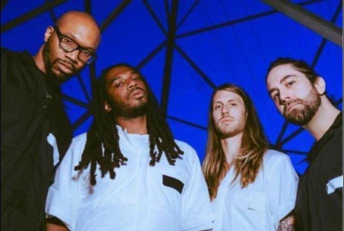 The OBGMs looking down at the camera, with a dark blue sky and beams behind them.