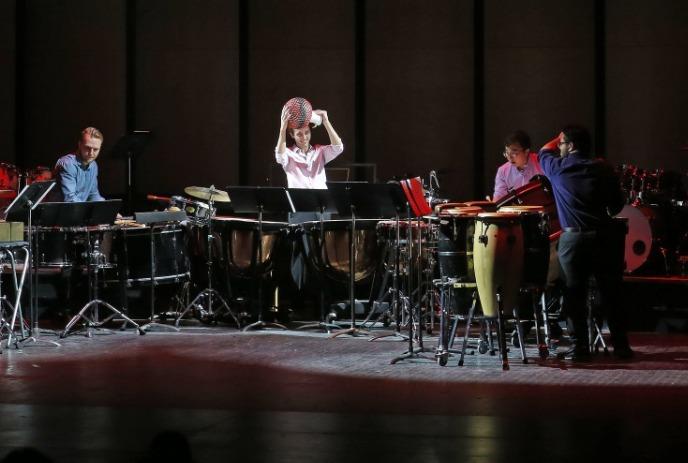 Four musicians perform on a dimly lit stage with various percussion instruments.
