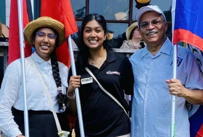 Three smiling people pose with colorful flags outdoors, together at Emancipation Day Celebration.