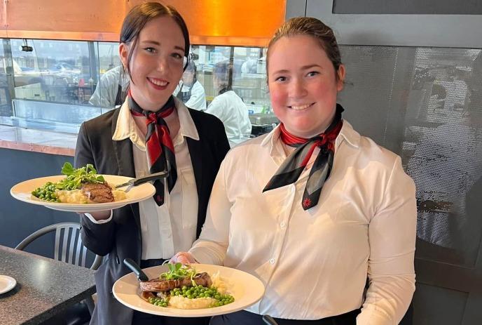 Two flight services students holding plates of food in their hands inside the restaurant.
