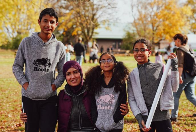Four people of different age groups gather together for a fall picture with yellow leaves on the trees.