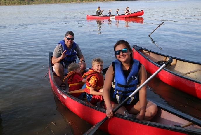 A mom, dad, and two small boys in a red canoe, smiling while on a lake.