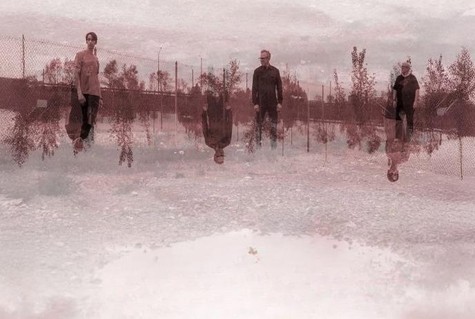 Three people stand on a gravel path, mirrored below in sepia tones, evoking reflection.