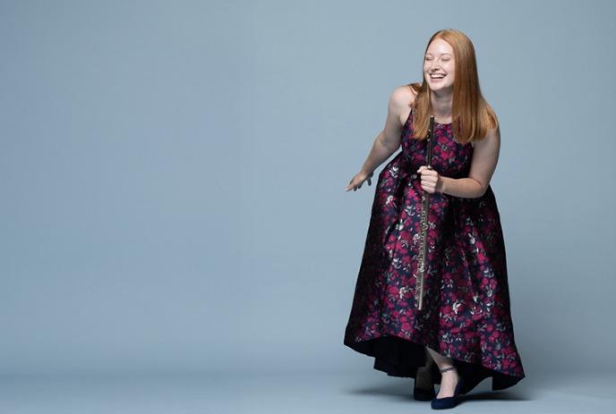 Gillian Derer wearing a dress and smiling, posing against a blueish grey background.