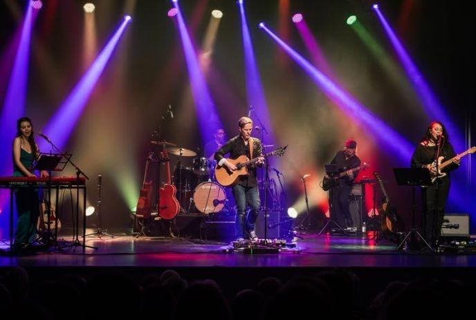 The Classic Troubadours Band playing on a stage with purple, blue and red lights all over.