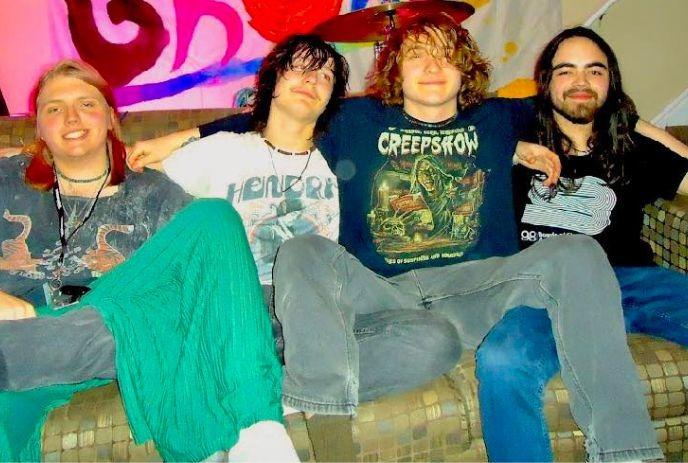 Four artists sitting on a couch posing for a picture.
