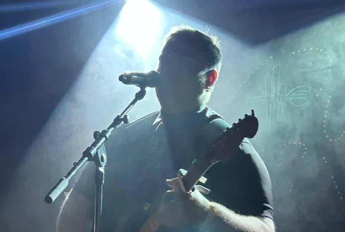 Silhouetted guitarist performs onstage with bright backlight and drifting fog creating dramatic concert mood.