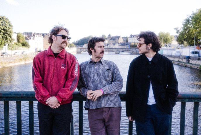 Three members of the band The Grogans standing on a bridge overlooking a river.