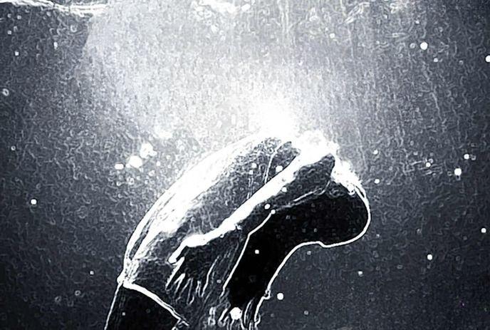 A person dives underwater with light rays and bubbles surrounding them in a dark aquatic scene.