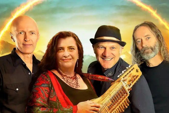 The 4 band members of Sultans of String stand beside one another posing for the camera, with mountains in the background.